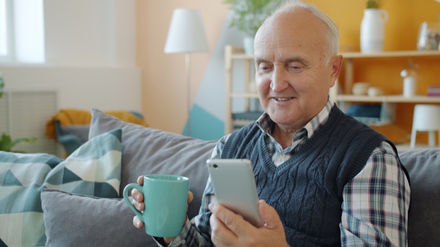 A smiling older man with his morning cuppa taking his check-in call